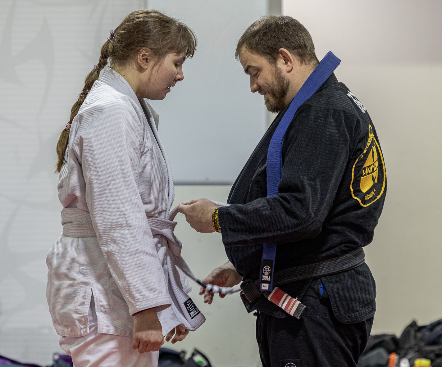 BJJ black belt untying a new blue belt's white belt. The blue belt is wrapped around the coach's shoulder.