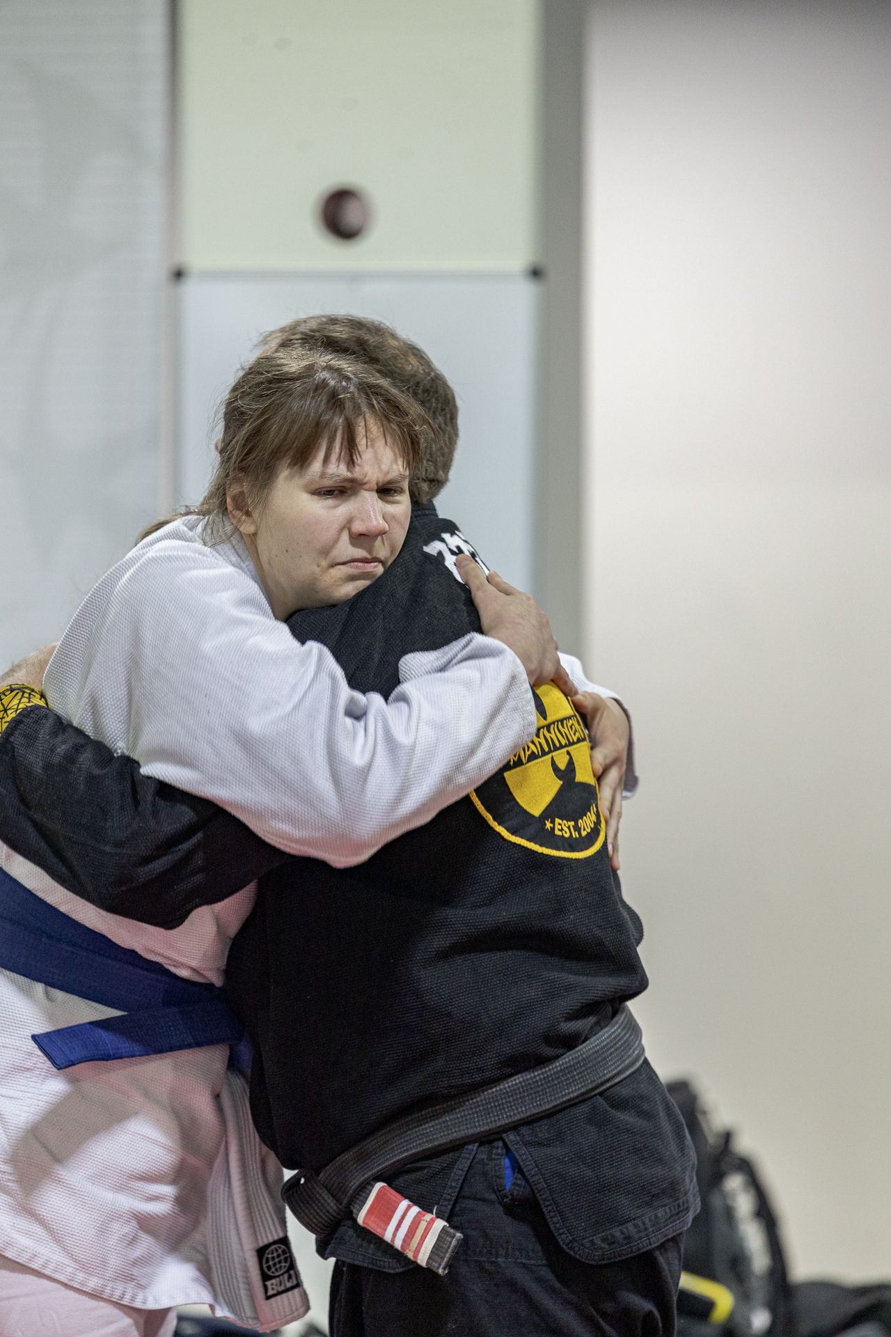 BJJ black belt and new blue belt embrace. Blue belt's face has distorted by how moved they are.