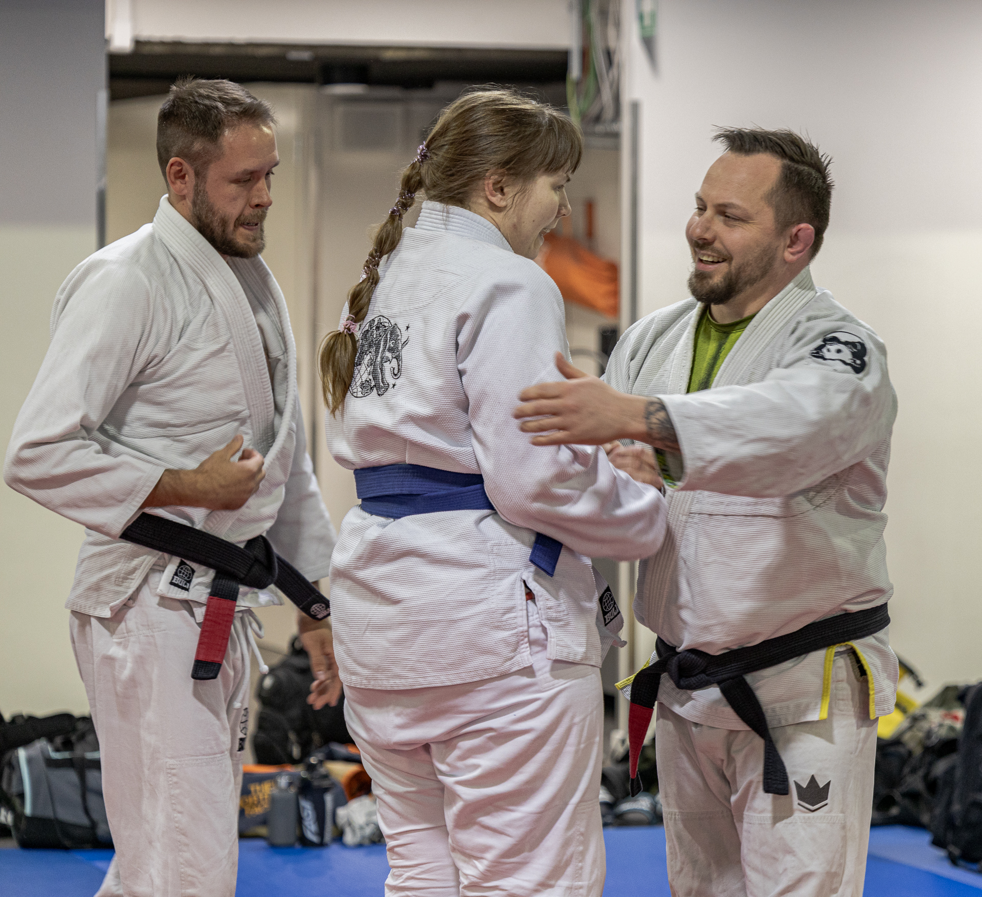 Two BJJ black belts congratulate a new BJJ blue belt.